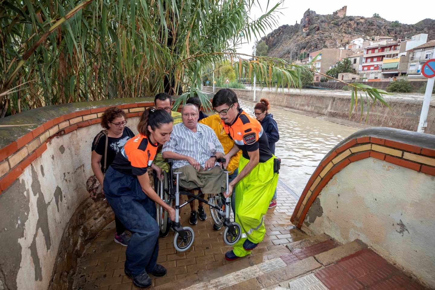 Voluntarios de protección civil trasladan a un hombre en silla de ruedas tras las intensas lluvias esta tarde en el barrio de Runes, Blanca, (Murcia)