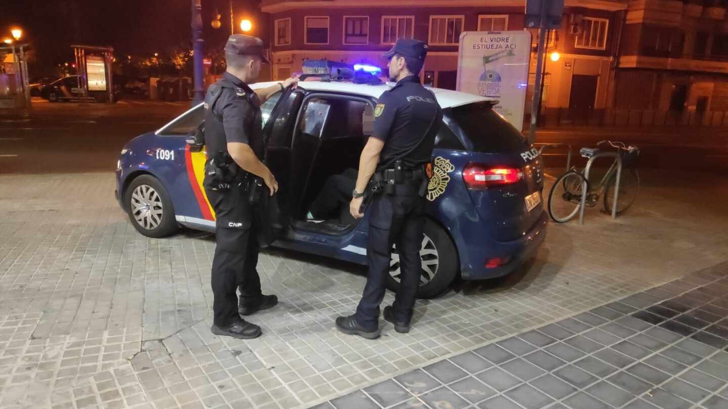 Dos miembros de la Policía Nacional junto a un coche patrulla.