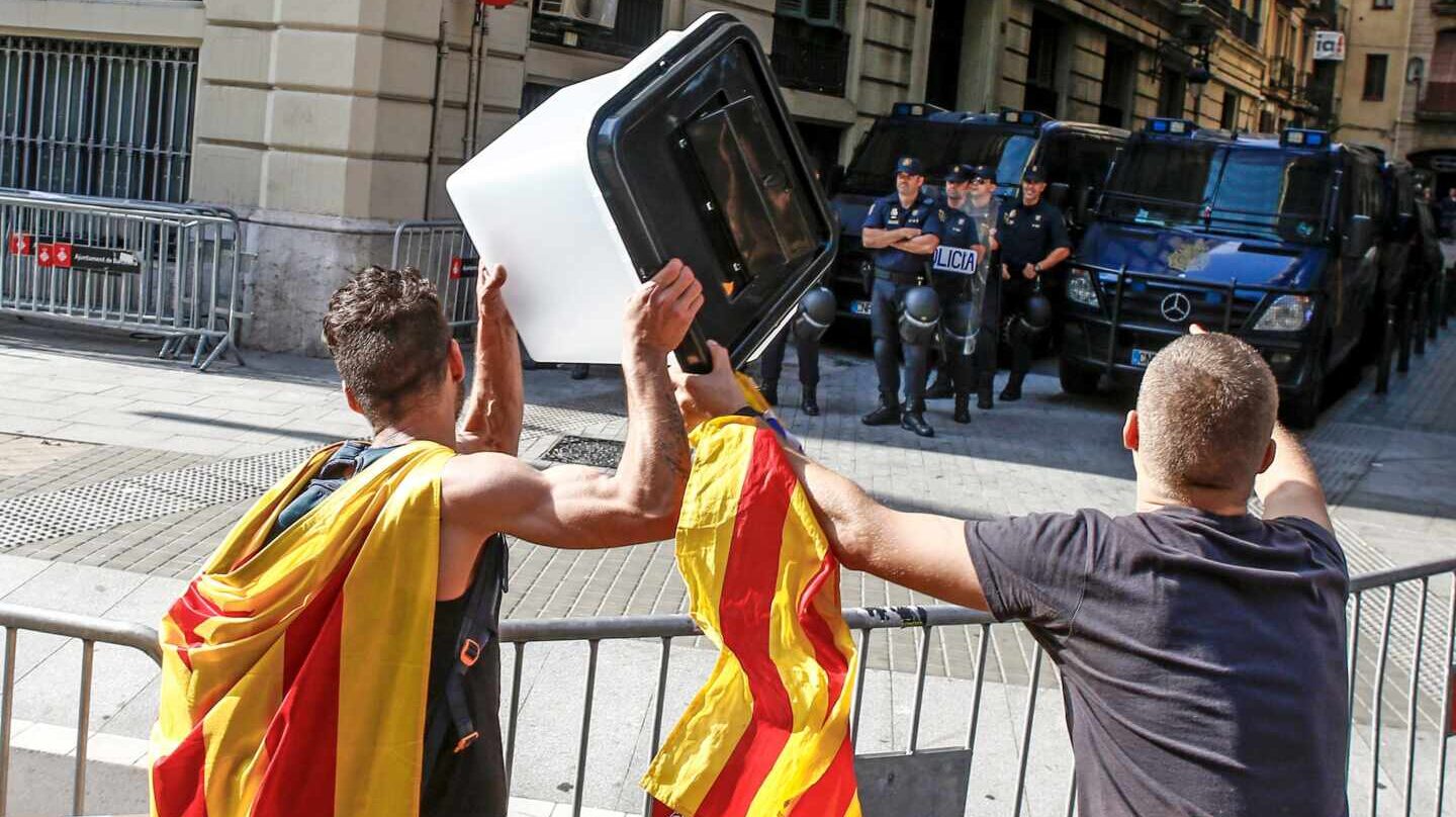 Dos jóvenes independentistas muestran esta semana una urna empleada el 1-O a los policías nacionales apostados ante la Jefatura Superior de Barcelona.