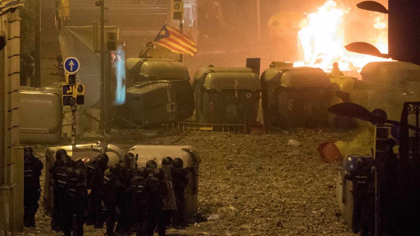 Policías nacionales, parapetados este viernes tras unos contenedores ante una de las barricadas levantadas por los violentos en Barcelona.