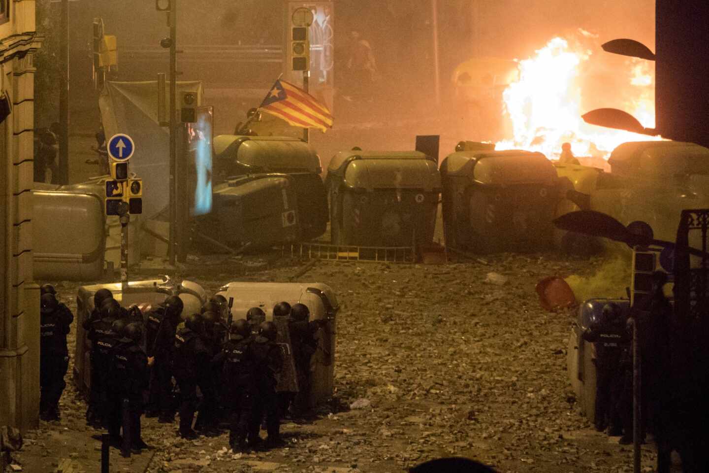 Policías nacionales, parapetados este viernes tras unos contenedores ante una de las barricadas levantadas por los violentos en Barcelona.