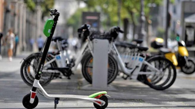 Un patinete de alquiler delante de una estación de bicis eléctricas.
