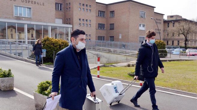 Dos personas con mascarillas caminan con equipos médicos portátiles en el exterior del Hospital Cívico Codogno