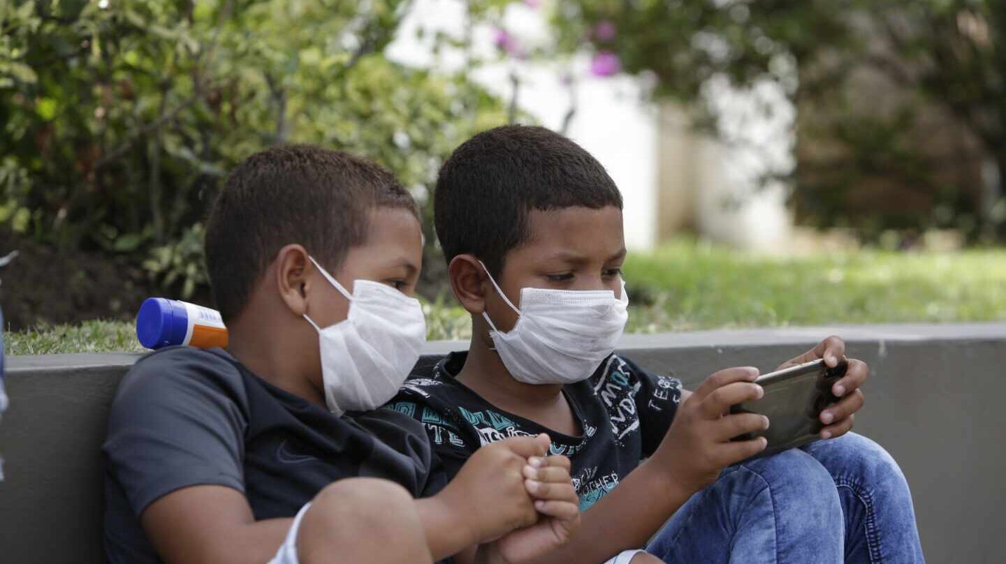 Dos niños con mascarillas juegan con un teléfono móvil en Panamá