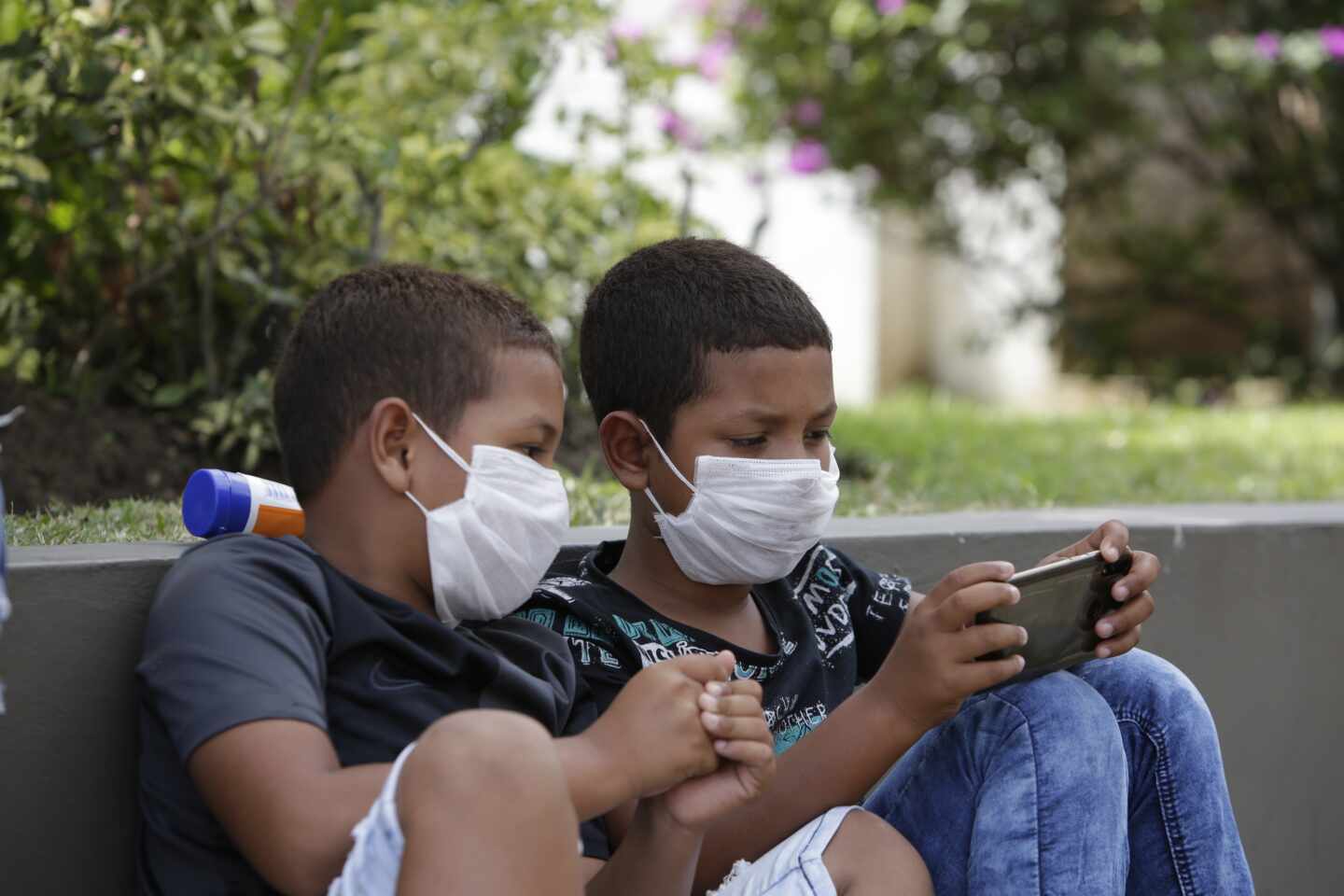 Dos niños con mascarillas juegan con un teléfono móvil en Panamá