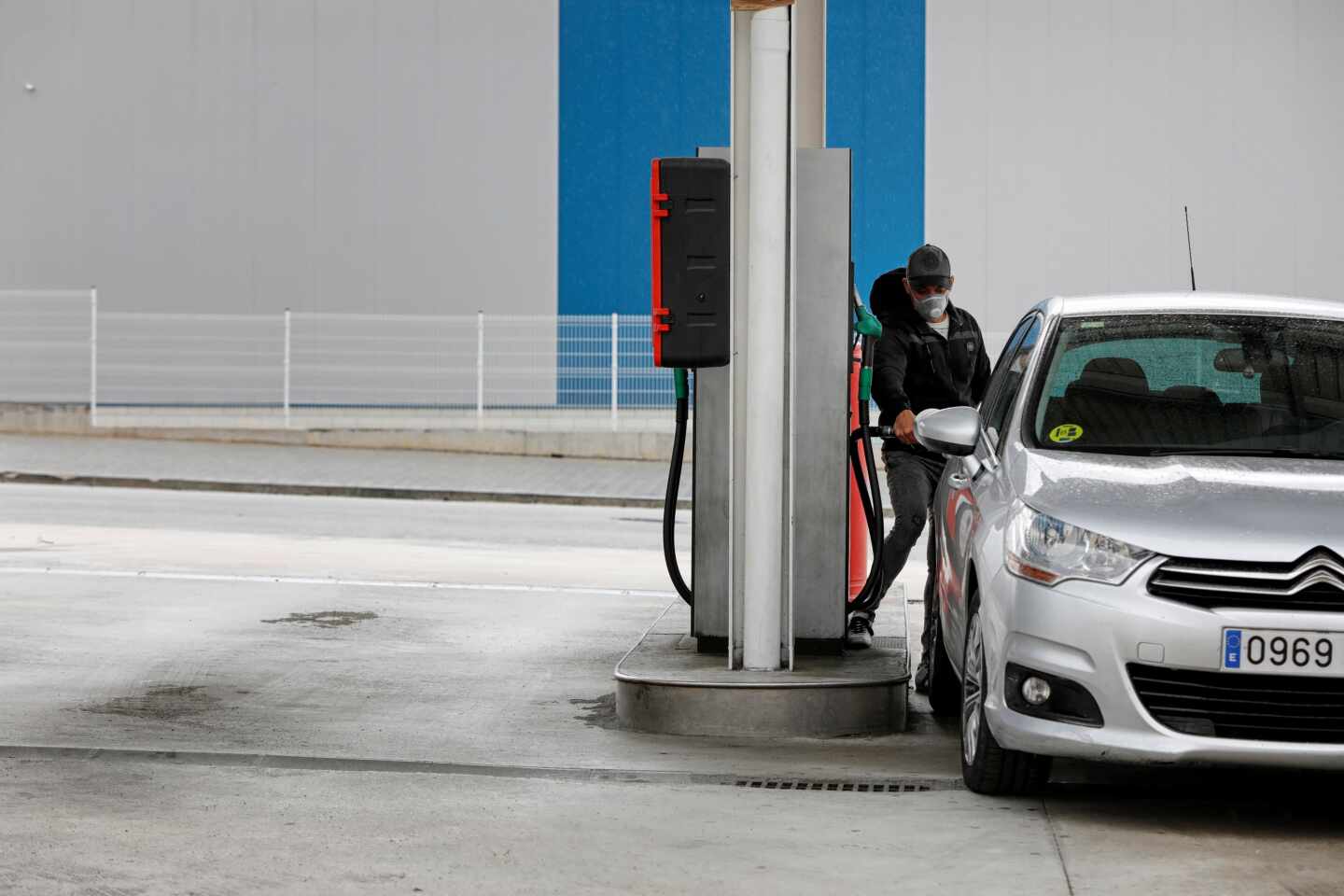 Un conductor con mascarilla reposta en una gasolinera.