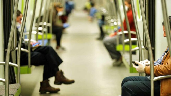 Dos hombres consultan sus teléfonos móviles en el transporte público.