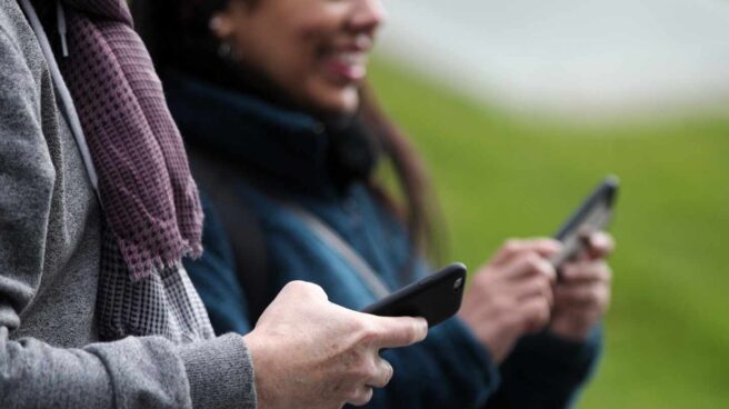 Dos paseantes utilizando su teléfono móvil.