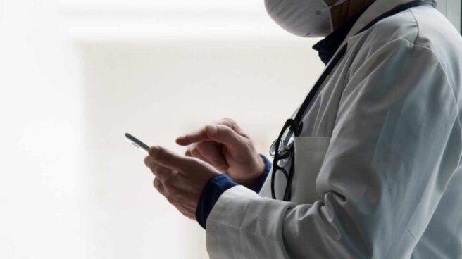 Un médico con mascarilla utiliza un móvil.