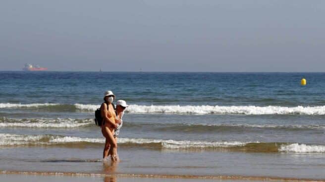 Dos bañistas con mascarilla en la playa de Gijón.