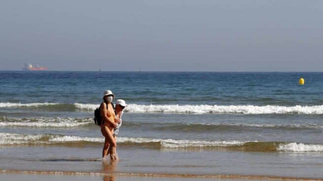 Dos bañistas con mascarilla en la playa de Gijón. Dos bañistas con mascarilla en la playa de Gijón.