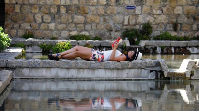 Una mujer lee tumbada junto a una fuente en una plaza de Córdoba.