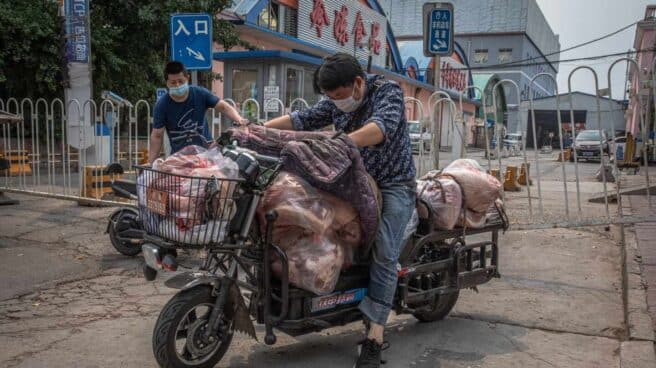 Unos hombres cargan una moto con carne de cerdo junto al mercado de Xinfadi, en China.