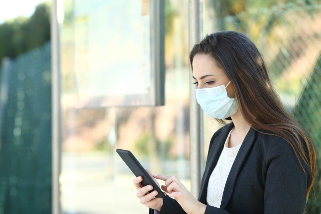 Una usuario utiliza su móvil en la calle con mascarilla.