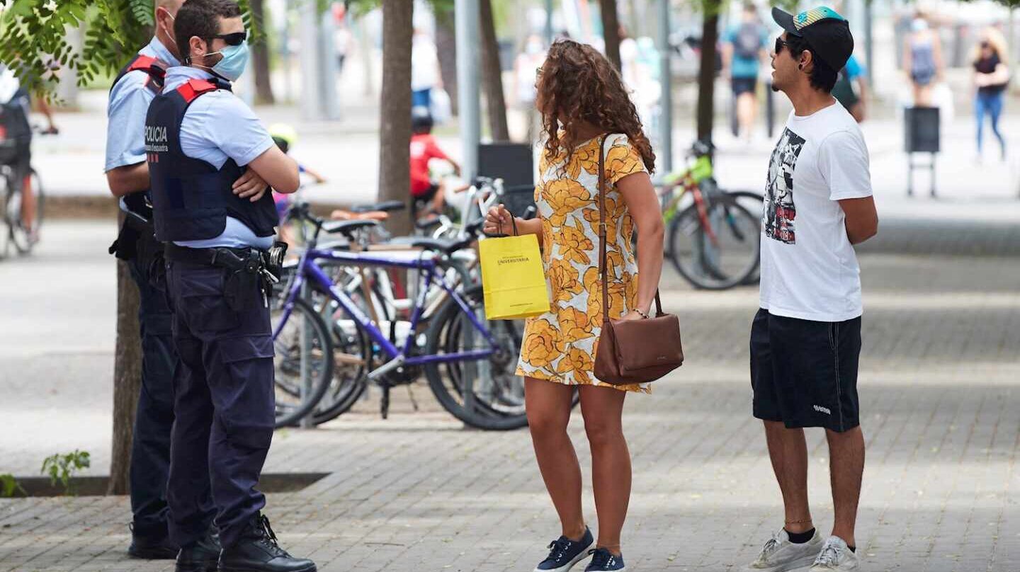 Unos agentes de los Mossos d'Esquadra informan a una pareja del uso obligatorio de la mascarilla, en Barcelona.