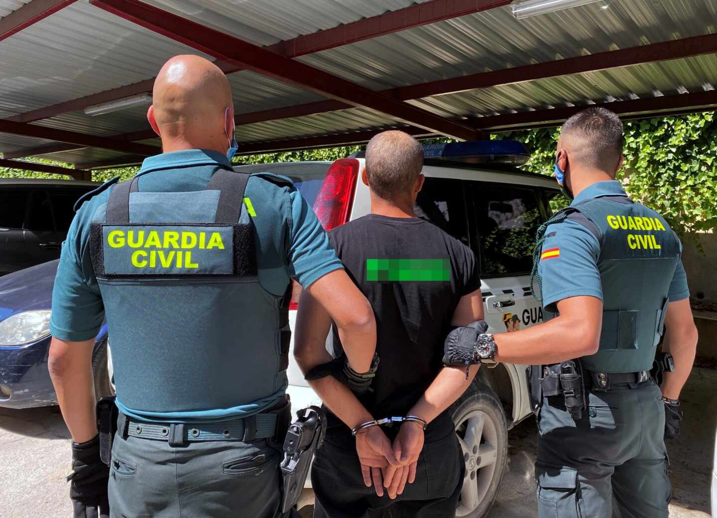 Una pareja de guardias civiles, provistos de chalecos antibala externos, conduciendo a un detenido.