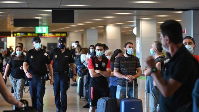 Policías en la T-1 del aeropuerto de Barajas junto a una hilera de pasajeros.