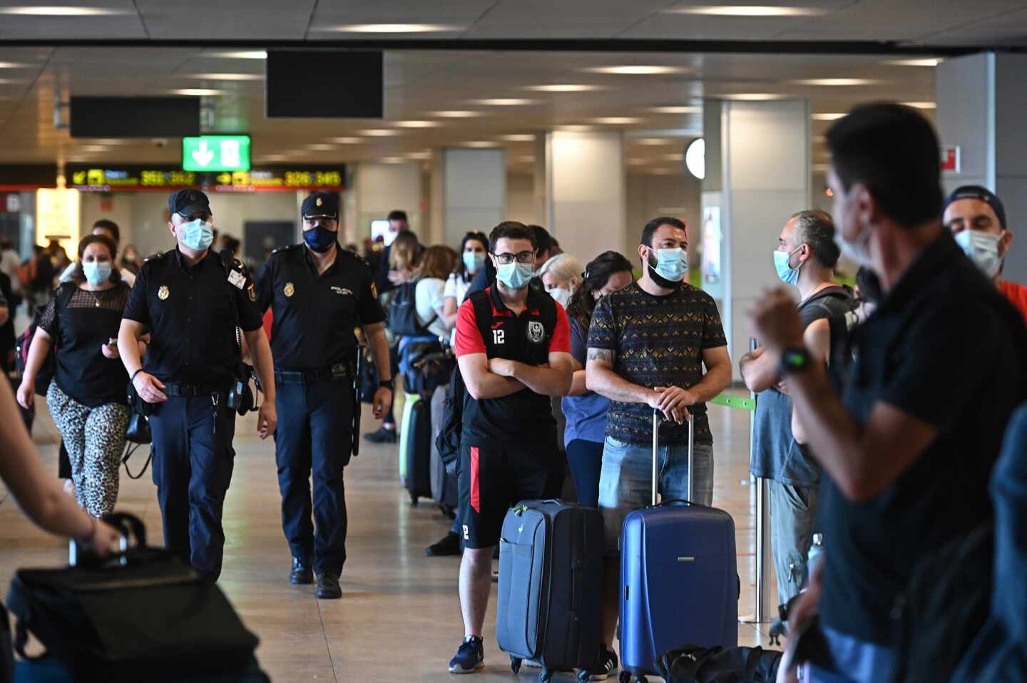 Policías en la T-1 del aeropuerto de Barajas junto a una hilera de pasajeros.