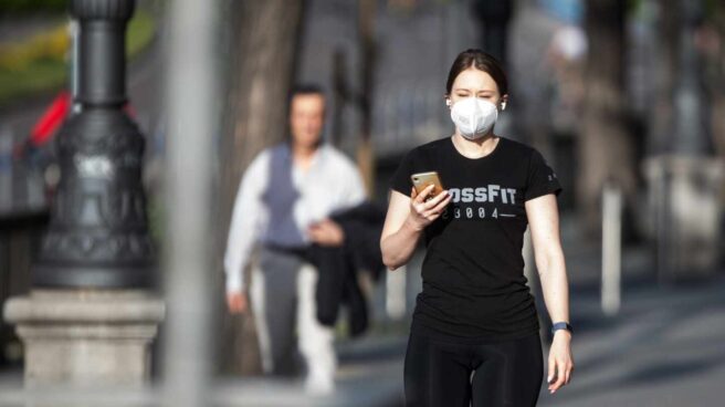 Una viandante con mascarilla utiliza su teléfono móvil.