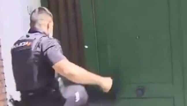 Un policía trata de forzar a patadas la puerta de una vivienda ocupada.