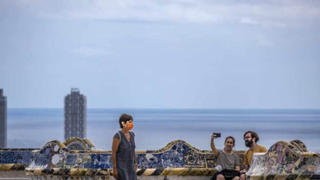 Una mujer camina junto a una pareja tomando un selfie en el Parque Güell. Una mujer camina junto a una pareja tomando un selfie en el Parque Güell.
