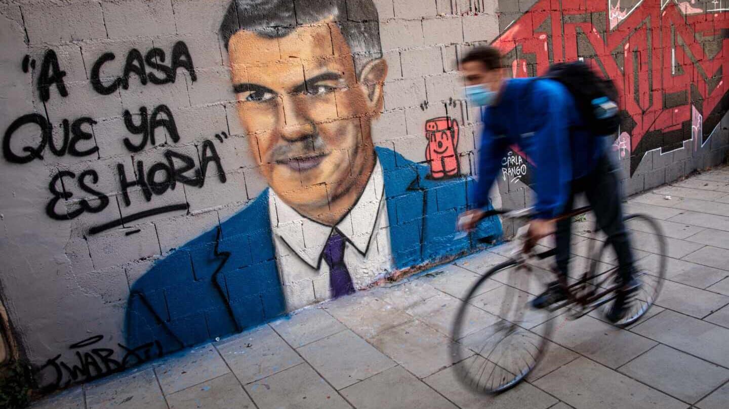 Una persona pasa frente a un mural de J.Warx, donde aparece Pedro Sánchez y una frase que éste tuiteó en 2012.