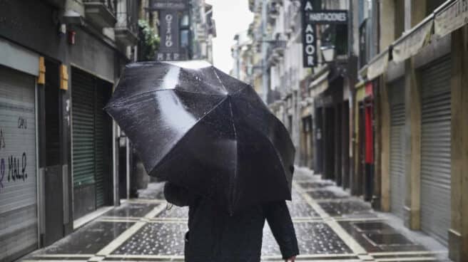 Un hombre camina protegiéndose con un paraguas por la lluvia por el casco viejo de Pamplona.