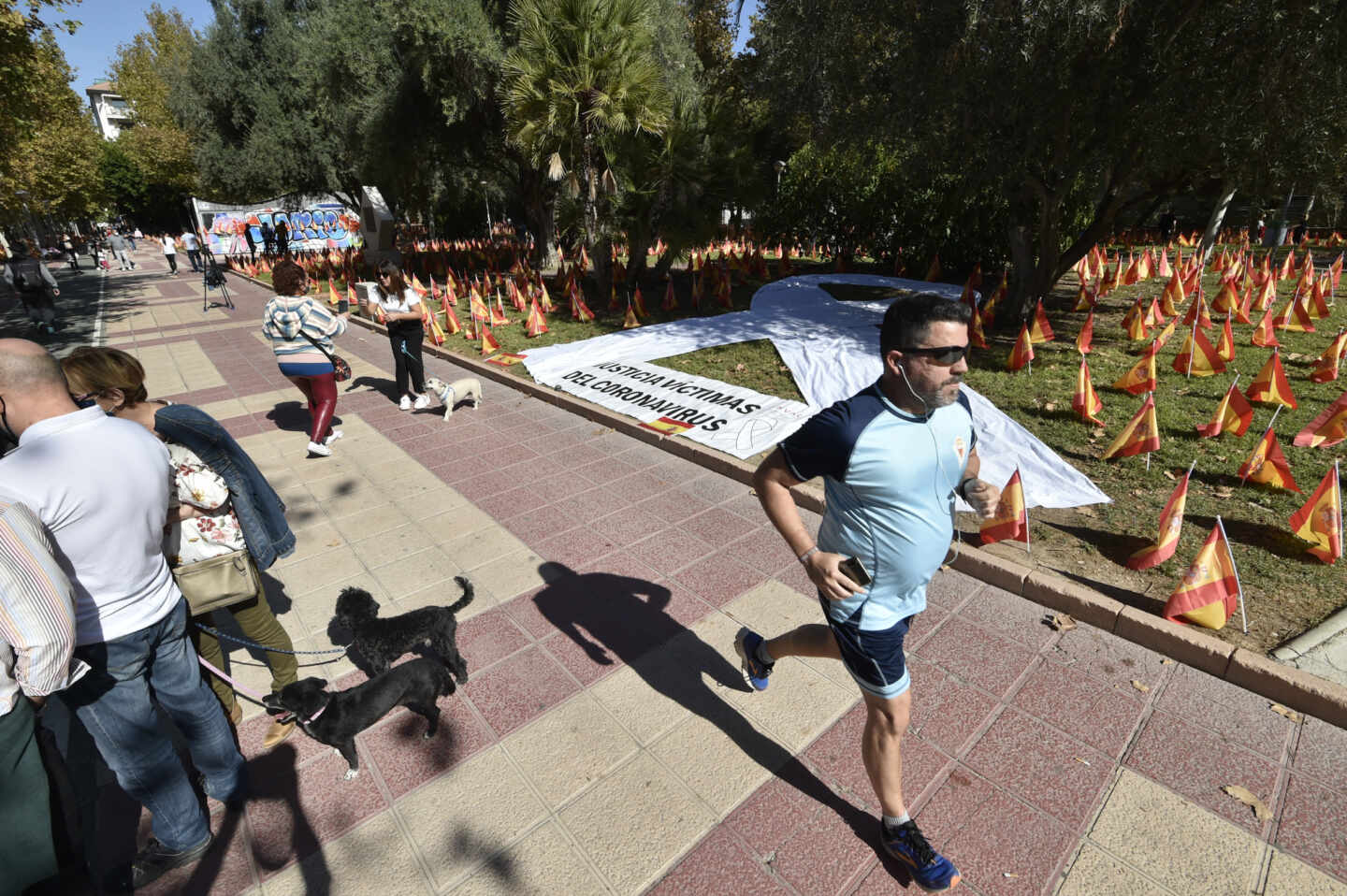 Varias personas pasean junto a las banderas de España en el Parque Isidoro Medina, en Murcia.