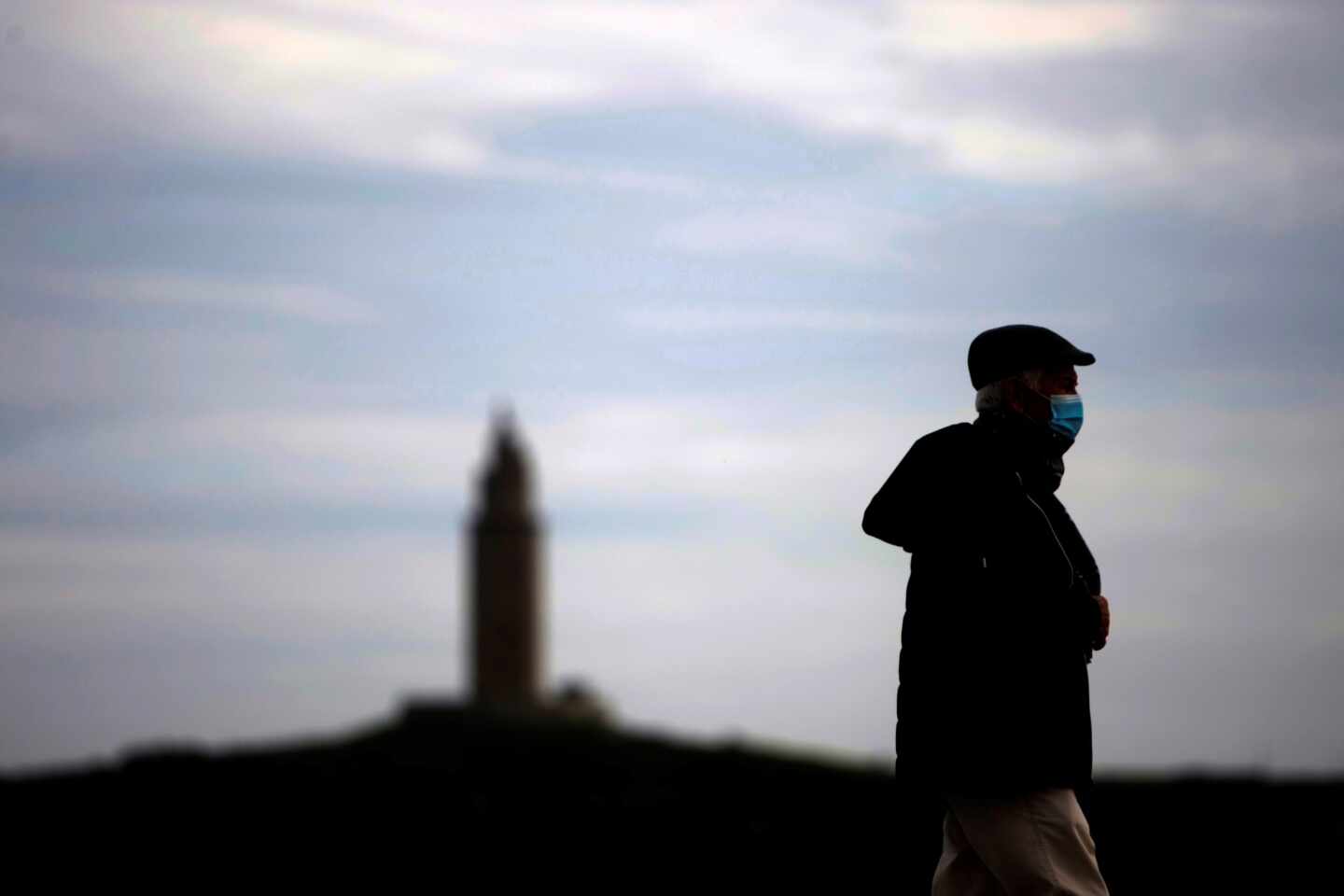 Un hombre camina por el paseo marítimo de A Coruña, con la Torre de Hércules al fondo.