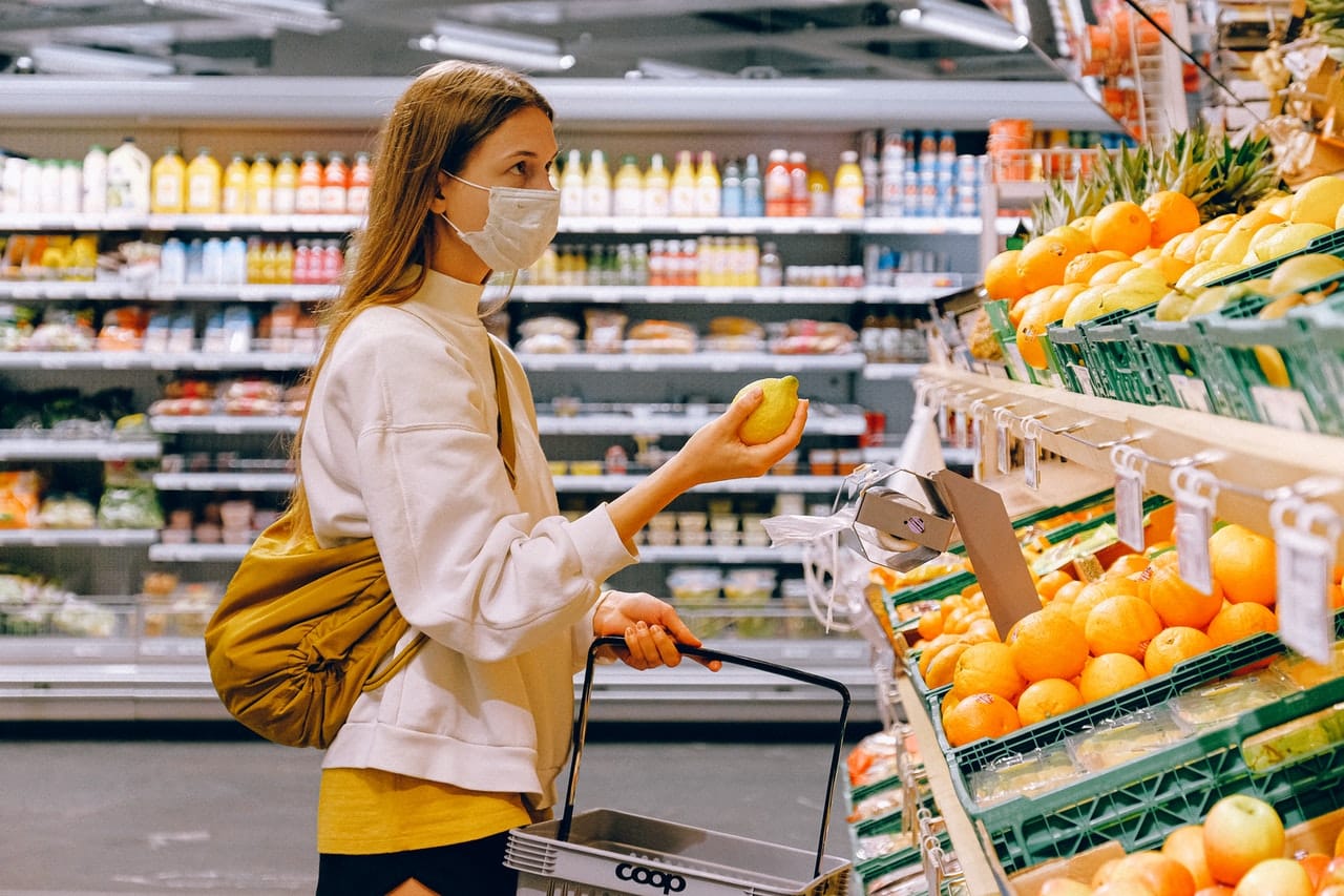 Una mujer con mascarilla sostiene una limón en un supermercado