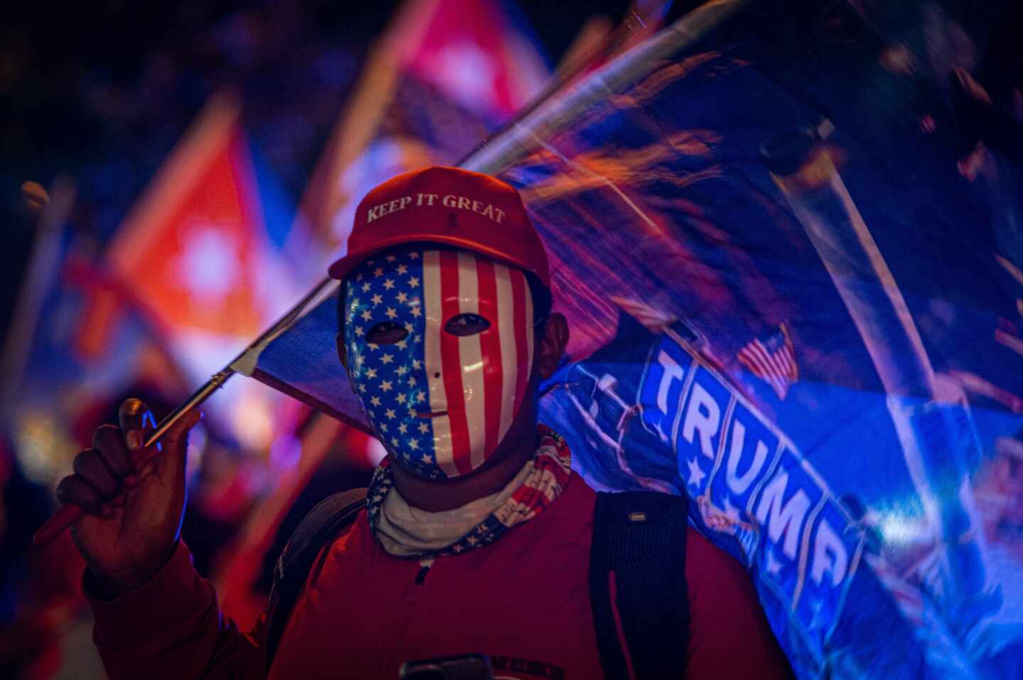 Un simpatizante de Donald Trump viste careta con la bandera estadounidense y una gorra que dice "Mantén (América) grandiosa" mientras espera los resultados de las elecciones presidenciales en Miami