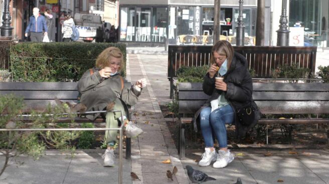 Dos mujeres toman café en una plaza de Gijón.