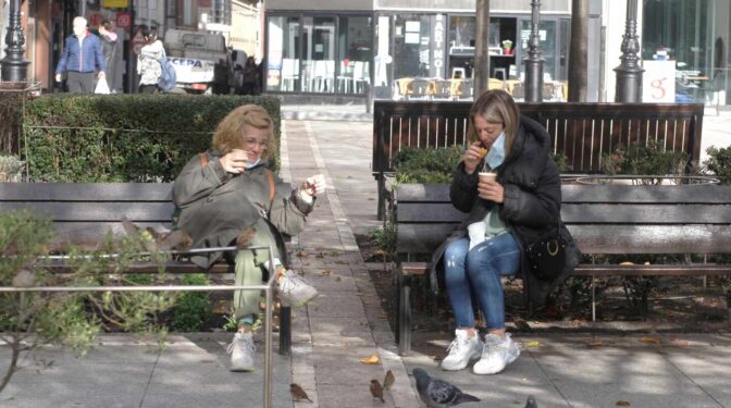 Dos mujeres toman café en una plaza de Gijón.