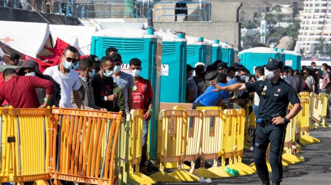 Un policía nacional se dirige a un grupo de inmigrantes en el puerto de Arguineguín.