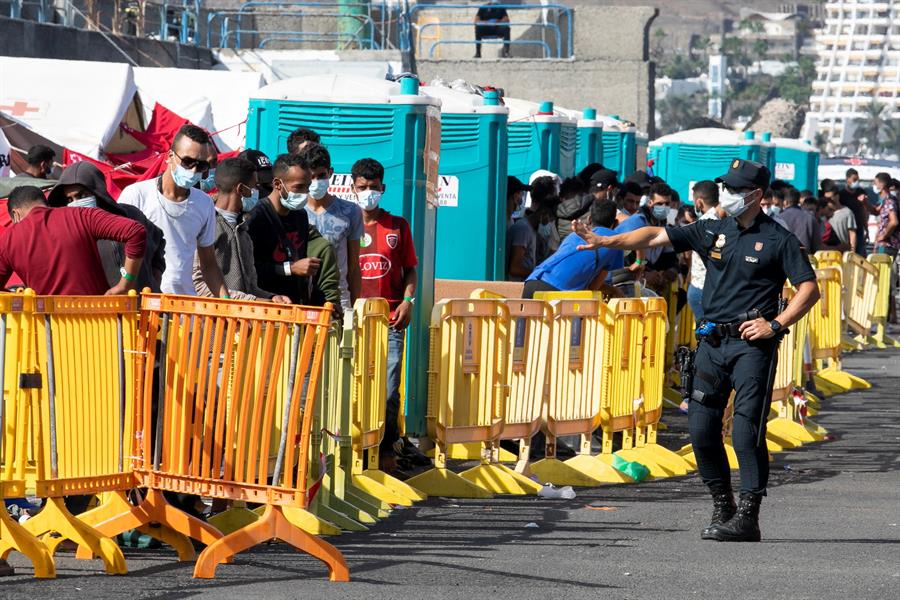 Un policía nacional se dirige a un grupo de inmigrantes en el puerto de Arguineguín.