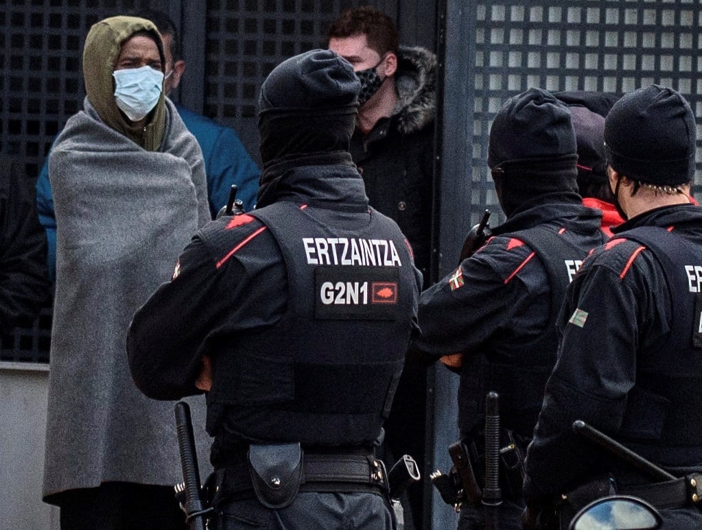 Un asistente a la fiesta (izq) aguarda junto a agentes de la Ertzaintza este lunes durante el proceso de identificación de los 67 asistentes a una fiesta celebrada la pasada en la hospedería de un convento de Derio (Bizkaia).