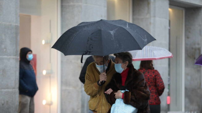 Dos personas pasean protegidas con paraguas por el centro de la capital, en Madrid.