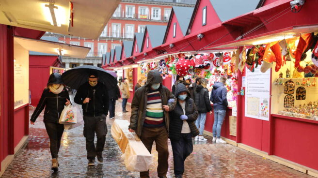 Personas protegidas por paraguas caminan por el mercadillo navideño de la Plaza Mayor, en Madrid.