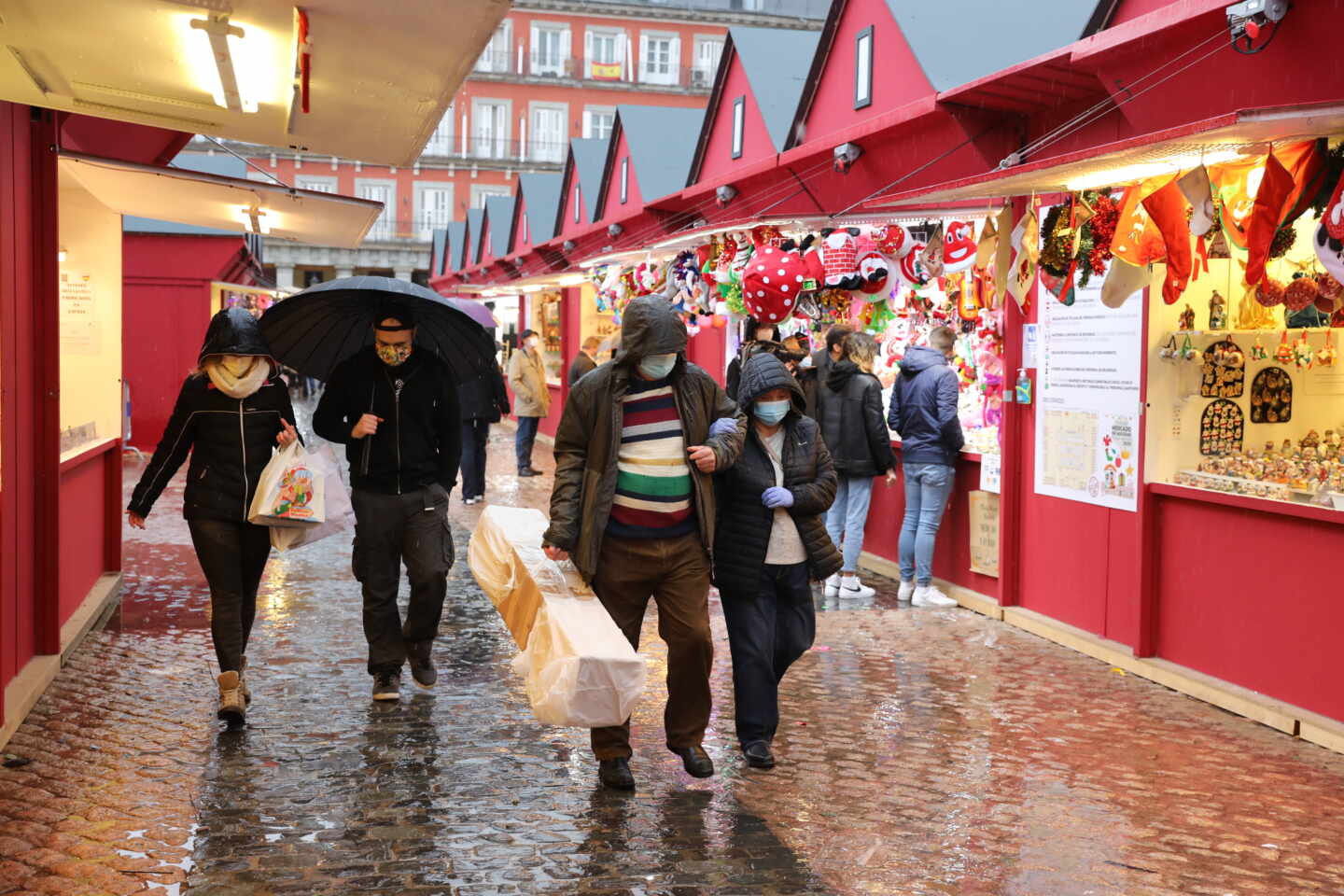 Personas protegidas por paraguas caminan por el mercadillo navideño de la Plaza Mayor, en Madrid.