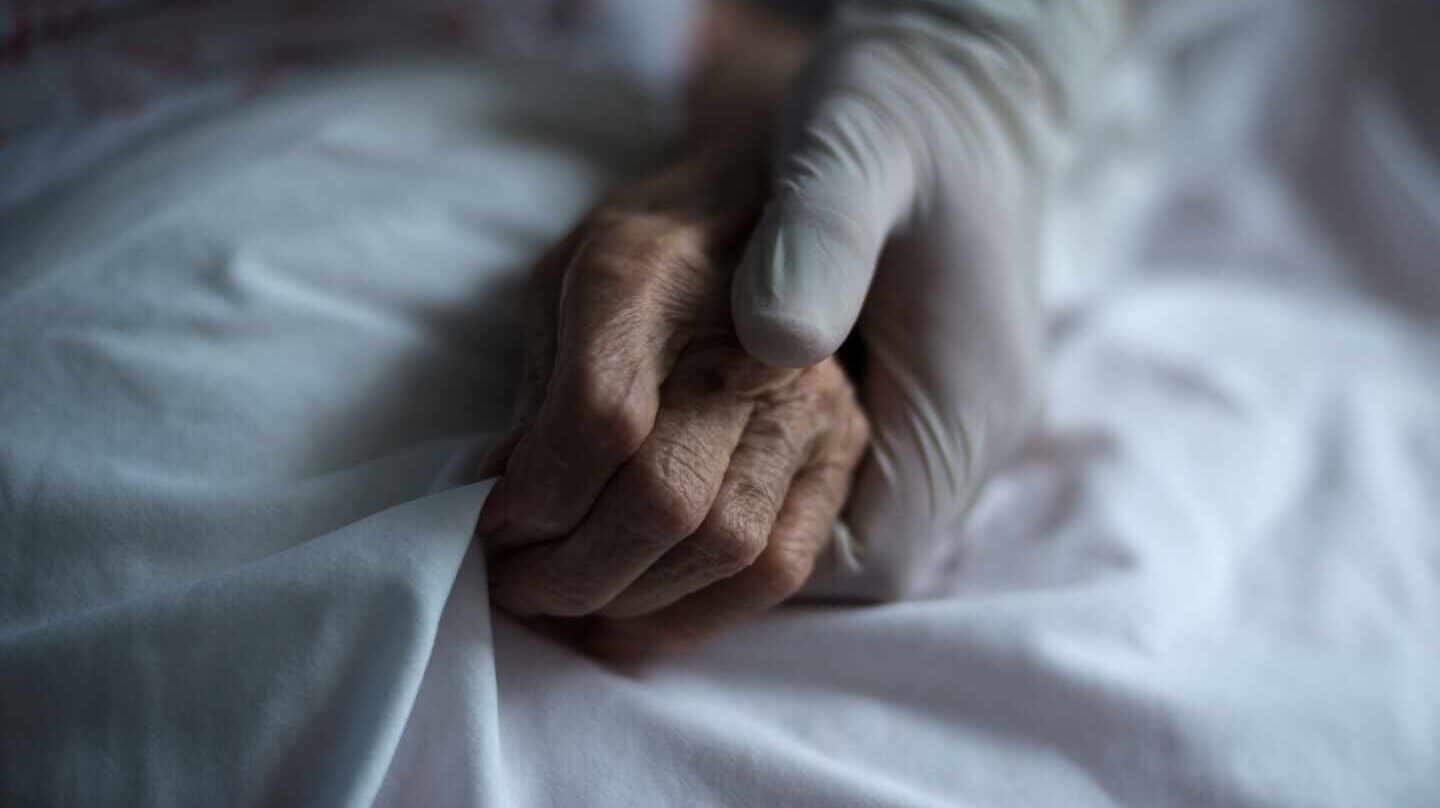 Una trabajadora de una residencia sujeta la mano de una anciana.
