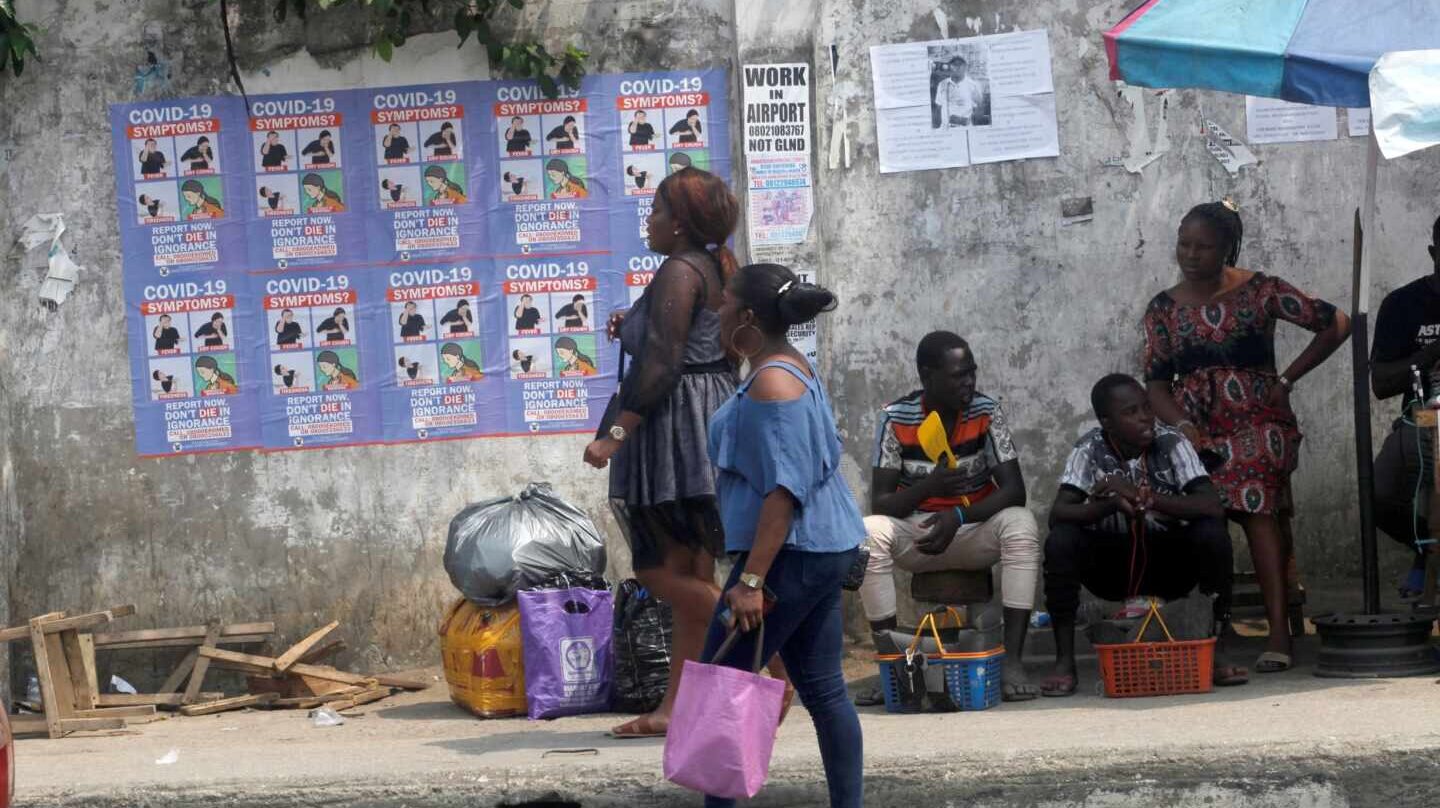 Varias personas caminan por Lagos (Nigeria), ante varios carteles que alertan de los síntomas del coronavirus