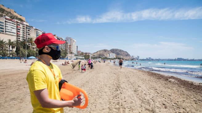 Un socorrista protegido con mascarilla vigila la Playa del Postiguet, en Alicante.