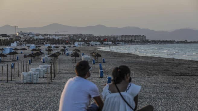 Estas son las cinco medidas sanitarias que debe cumplir en las playas valencianas Dos jóvenes sentados contemplan la playa de la Malvarrosa, en Valencia.