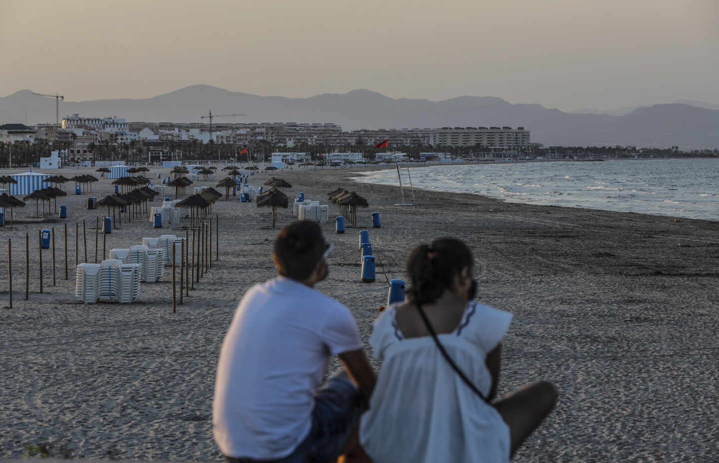 Dos jóvenes sentados contemplan la playa de la Malvarrosa, en Valencia.