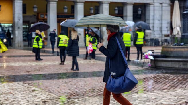 Una mujer camina protegida por un paraguas en la Plaza Mayor de Madrid.