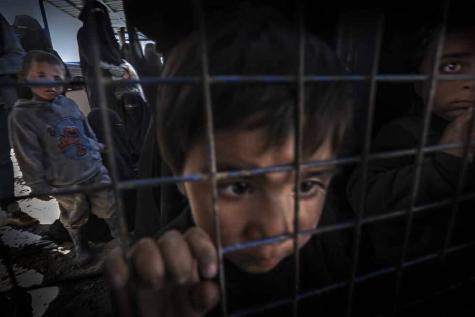 Un niño sirio observa a través de una verja en un campo de refugiados