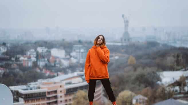 young-woman-in-an-orange-jacket-poses-on-the-roof-of-building-in-the-city-center