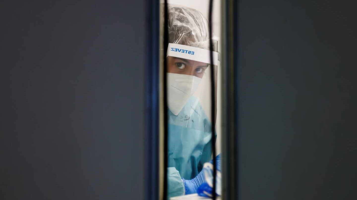 Un médico se asoma por la puerta de una sala de un aeropuerto donde toma muestras.