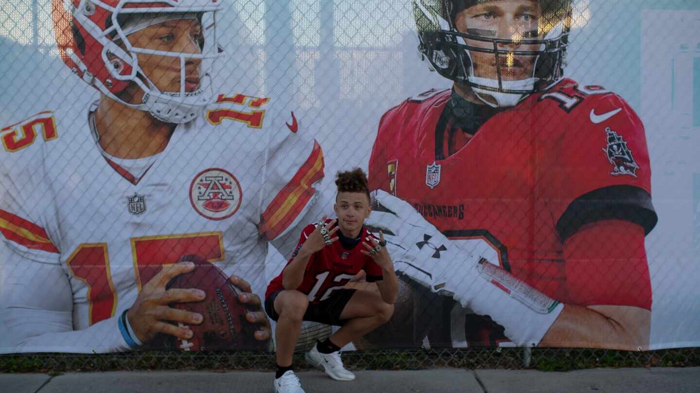 Un aficionado posa ante un cartel de Patrick Mahomes (izquierda) y Tom Brady (derecha).