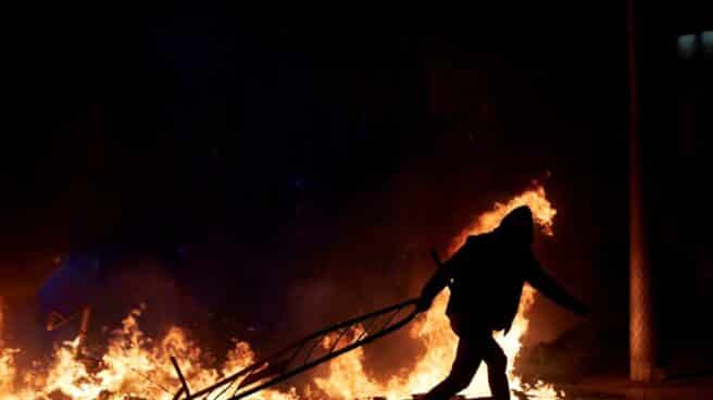 Un manifestante lanza una valla a la barricada en llamas en la calle Aragó, anoche en Barcelona durante las protestas por la detención de Pablo Hasél.